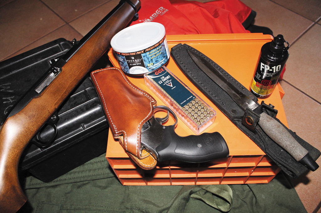 Firearms can provide peace of mind, pest control, and the occasional meal. Pictured here are a 10-shot Smith & Wesson 617 revolver, a brick of .22 Short cartridges, a Ruger 10/22 rifle, and a nitrogen-sealed can of Federal .22LR ammo.