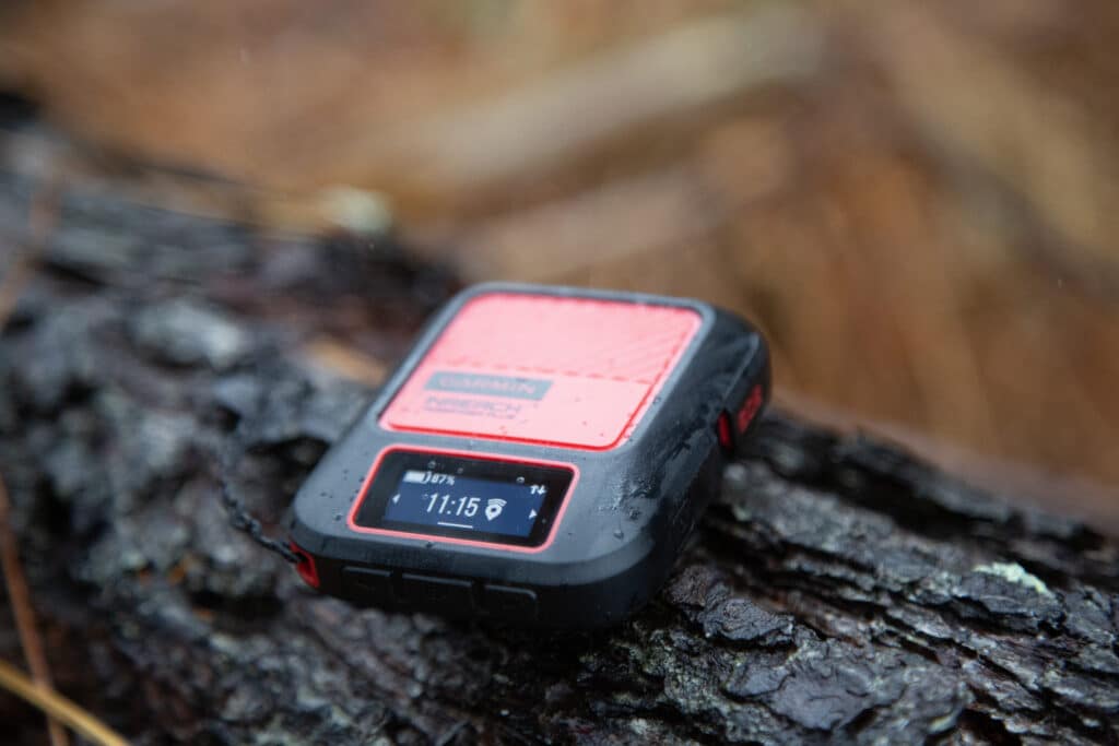 a Garmin Inreach sitting on a log in the forest.